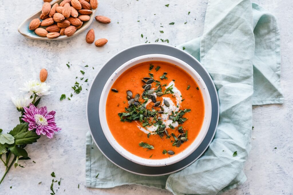 healthy vegan soup recipes; bowl of creamy tomato soup topped with herbs and cream on beautiful table