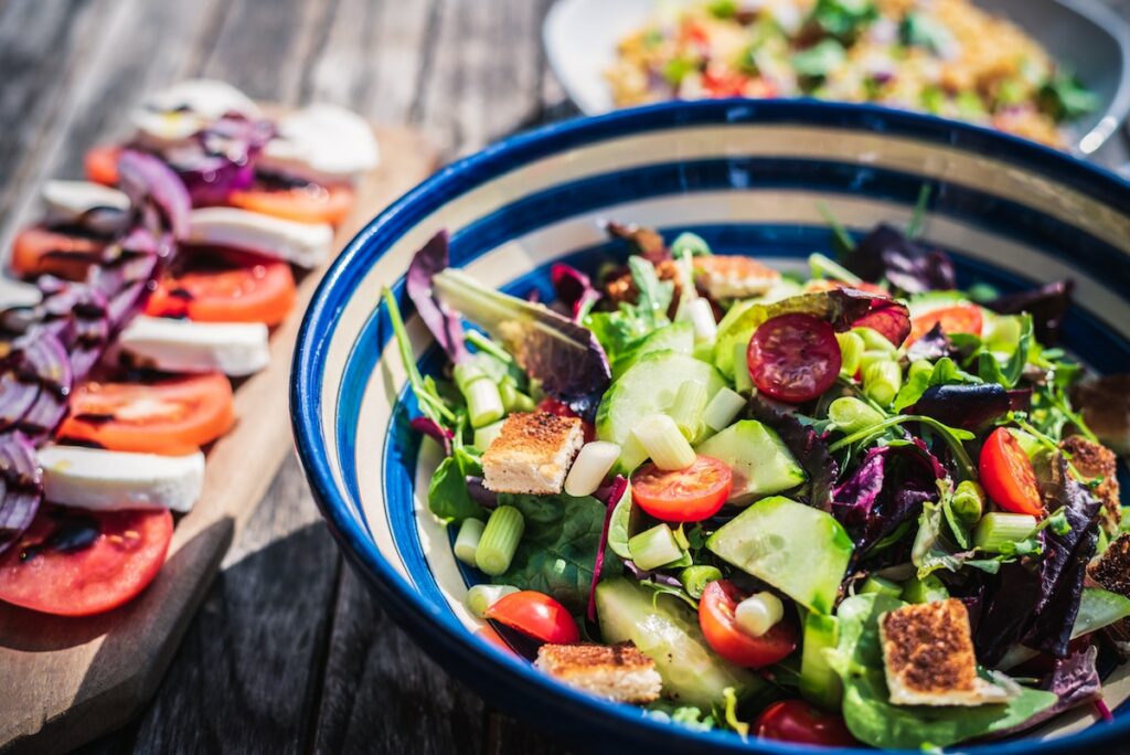 healthy salad in bowl, mozzarella and tomatoes on cutting board, low-carb lunches concept