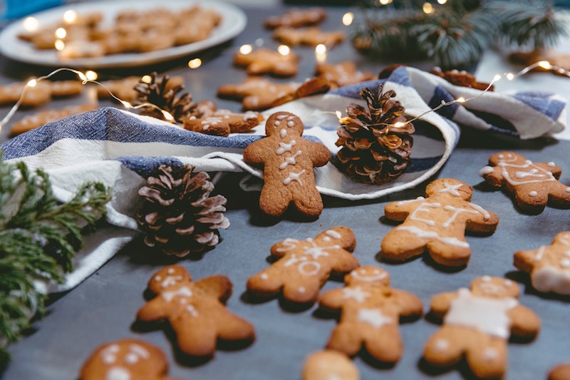 photo of gingerbread men cookies spread out on festive table with pinecones and lights; healthy Christmas cookies recipes concept