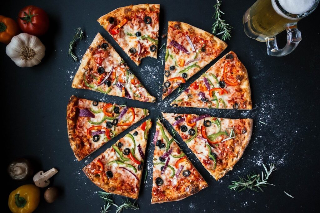 veggie pizza on dark surface surrounding by veggies, garlic, rosemary